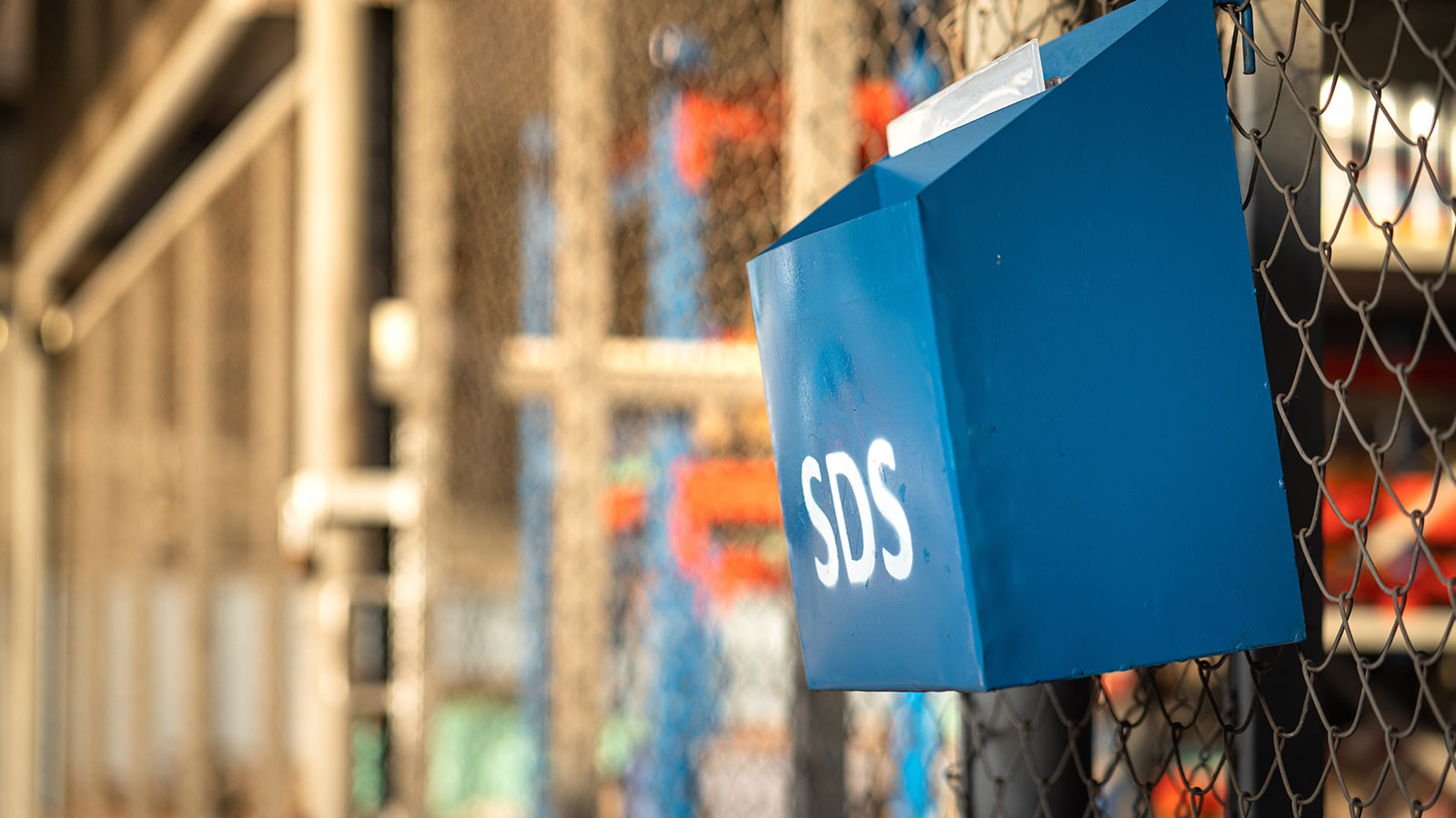 A blue box, hanging on a chain link fence containing safety data sheets